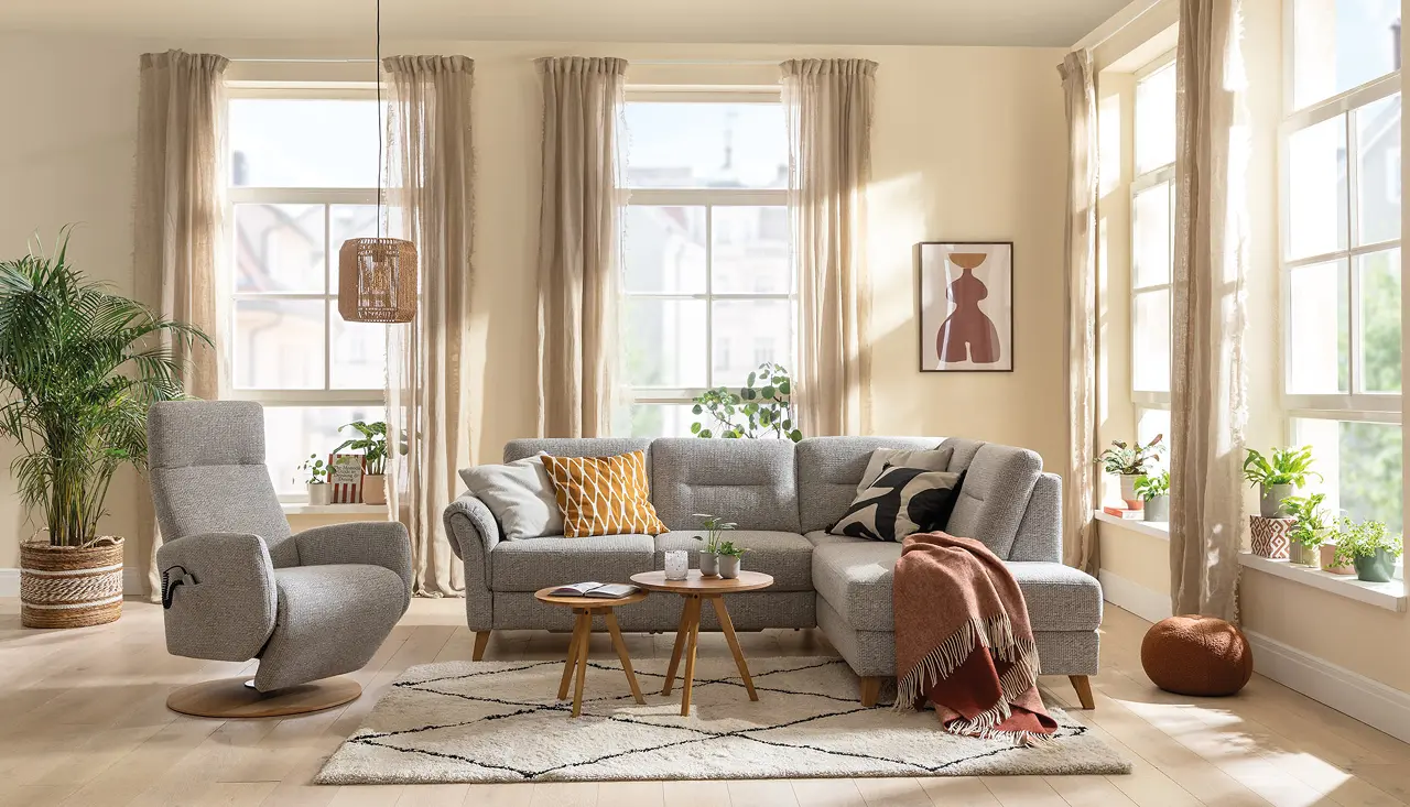 Helles Wohnzimmer mit grauem Ecksofa und Relaxsessel, dekoriert mit bunten Kissen, Pflanzen und Teppich im skandinavischen Stil – modernes Sofa-Design für gemütliches Wohnen.